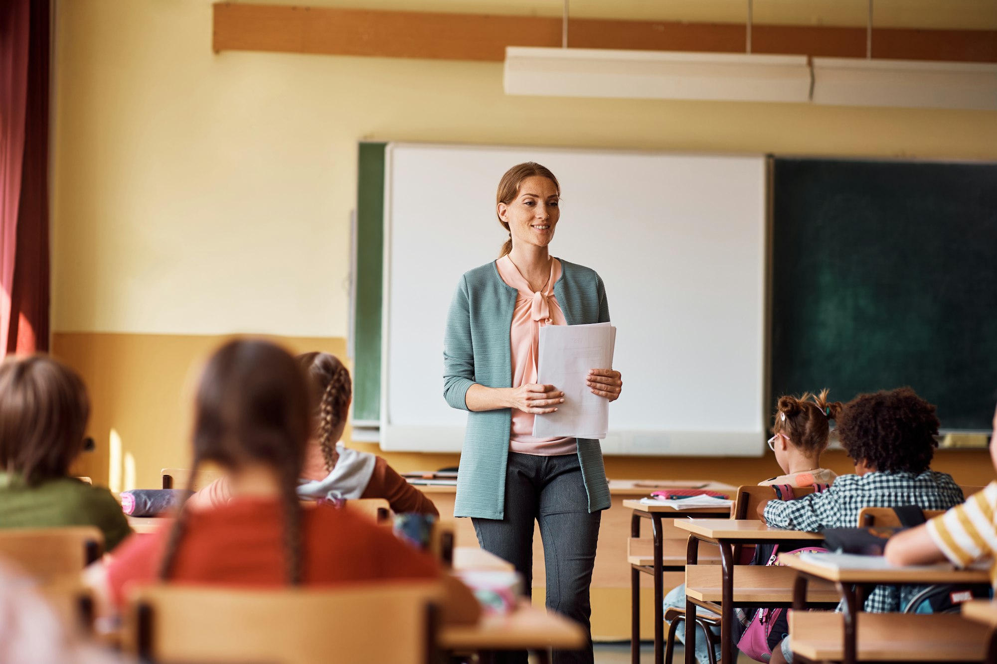 Happy elementary school teacher giving lecture to her students in the classroom.